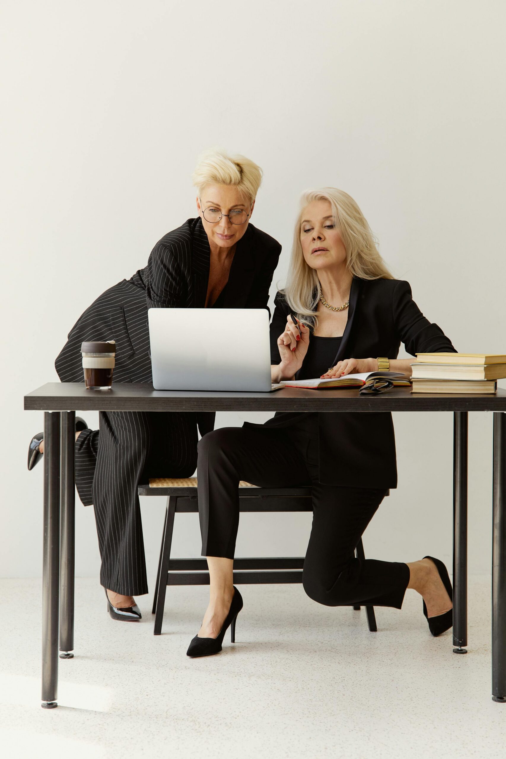Two senior businesswomen working together on a laptop at a table.